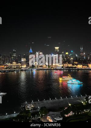 Skyline von Shanghai bei Nacht mit dem Oriental Pearl Tower, der in Blau leuchtet, Lichter reflektieren über dem Huangpu River. Stockfoto