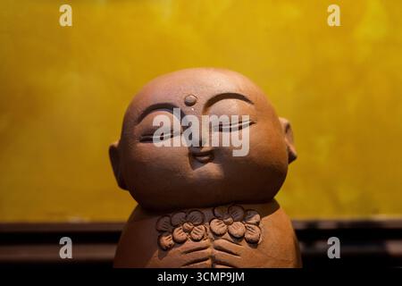 Nahaufnahme einer friedlichen Buddha-Statue aus Ton mit Blumenschnitzereien, die vor einem warmen gelben Hintergrund stehen und Gelassenheit und Achtsamkeit symbolisieren. Stockfoto