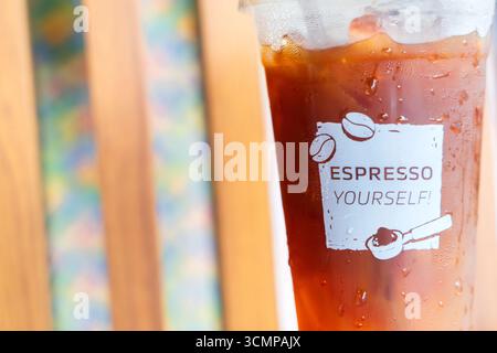 Nahaufnahme von Eiskaffee in einer Plastiktasse mit Kondenswasser, verspieltem „Espresso Yourself“-Text und Kaffeebohne-Design. Stockfoto