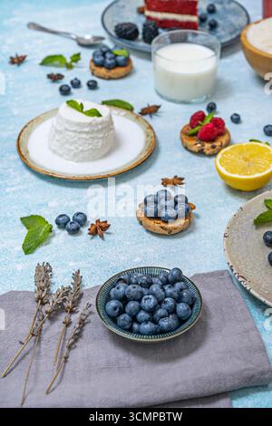 Bild eines Sommer-Imbisses: Eine Schüssel Hüttenkäse, Müsli und Heidelbeeren, neben einer süßen Limonade in einem Glas Stockfoto