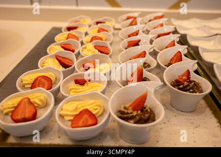 Ein Tablett mit Desserts mit Erdbeeren und Sahne. Die Desserts sind in weißen Schüsseln und optisch ansprechend angeordnet Stockfoto