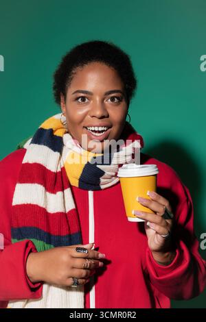 Eine stilvolle Black Woman in Übergröße trinkt Kaffee und trägt dabei einen herbstfarbenen Schal. Stockfoto