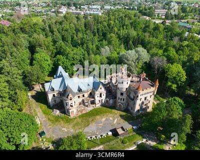 Aus der Vogelperspektive sehen Sie die baufällige und verlassene Burg von Chrapovitski in Muromzewo, umgeben von einem üppigen grünen Wald. Stockfoto
