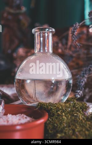 Nahaufnahme einer mystischen Tränkflasche umgeben von Moos, Kräutern und rituellem Salz auf einem spirituellen Wiccan-Altar. Stockfoto
