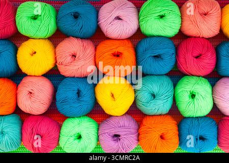 Viele bunte Garnknäuel auf einem gestrickten Stoff, Nahaufnahme. Stockfoto