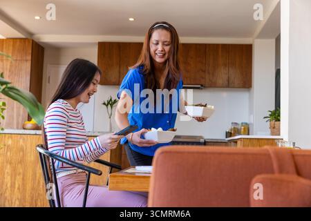 Asiatische Mutter und Tochter teilen ihre Mahlzeiten am Küchentisch mit Smartphone-Schalen Stockfoto