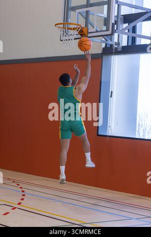 Männlicher Athlet springt mit Netz auf den Basketball, schießt Basketball auf dem Fitnessplatz mit Bodenlinien Stockfoto