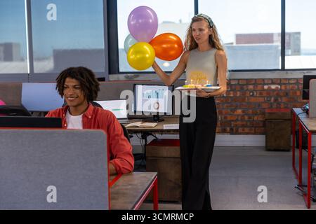 Verschiedene Kollegen feiern Geburtstag im Büro mit einem Laptop, der Ballons und Kuchen hält, Kopierraum Stockfoto