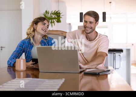 Ein Paar arbeitet am Laptop und überprüft das Smartphone am hölzernen Esstisch in der modernen Küche Stockfoto