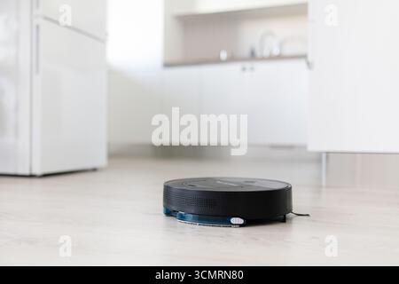 Schwarzer Roboter-Staubsauger, der auf Küchenboden arbeitet Stockfoto