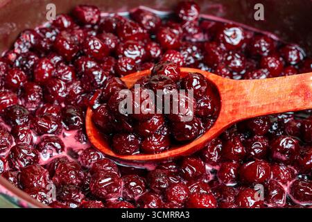 Zubereitung frisch gepflückter roter Kirschen mit Zucker zu Kirschmarmelade in einem Topf mit einem Holzlöffel, Nahaufnahme. Kochen Beeren Marmelade, hausgemachte Kekse Stockfoto