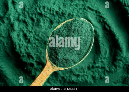 Haufen Sie grünes Spirulina-Algenpulver im Holzlöffel, Draufsicht auf grünem Spirulina-Pulver-Hintergrund. Nahrungsergänzungsmittel zur Verbesserung der Gesundheit. Seegras-Superf Stockfoto