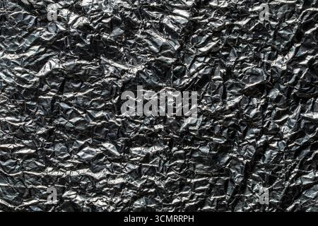 Hintergrund und Textur der gebrauchten zerknitterten Schokoladenfolie, Nahaufnahme, Draufsicht. Glänzende Aluminiumfolie ohne Schokoladenbonbons Stockfoto