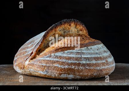 Runder Laib frisch gebackenes Sauerteigbrot auf hölzernem Schneidebrett, Nahaufnahme. Rustikales Sauerteigbrot. Kochen gesundes Sauerteigbrot zu Hause Stockfoto