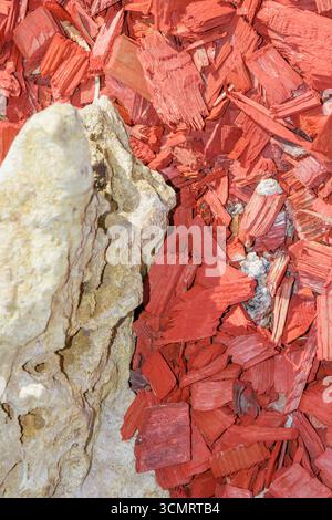 Detailliertes Makro eines rauen, strukturierten beigen Steins neben hellroten Holzmulchspänen, die den Kontrast zwischen Naturstein und Dekoraten hervorheben Stockfoto