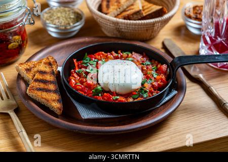 Köstlicher Shakshuka in der Pfanne zum Frühstück, Nahaufnahme. Hausgemachte Shakshuka aus pochiertem Ei, Zwiebeln, Paprika, roter Tomate und grüner Petersilie Stockfoto