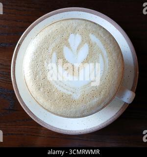 Ein Latte mit komplizierten Schaumkunstwerken, serviert in einem Keramikbecher auf einem Tisch Stockfoto