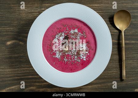 Süße Sommerkirschsuppe auf einem weißen Teller auf hölzernem Hintergrund, Nahaufnahme, Blick von oben. Ungarische kalte rote Kirschsuppe mit Joghurt oder Sahne, bestreut mit Stockfoto