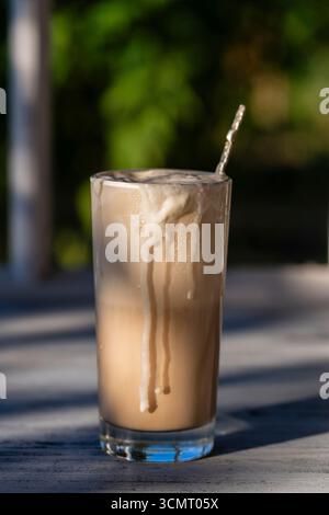 Ein Glas Kaffee mit Eis auf der Fensterbank neben dem Fenster. Kaltes Sommergetränk. Nahaufnahme Stockfoto