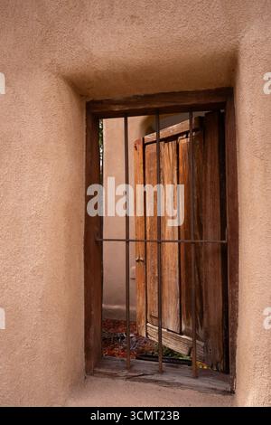 Große antike Holztür, die hinter einem Eisentor oder einer Tür in einem adobe-Haus in Santa Fe, New Mexico, USA, geöffnet ist, rechteckige Formen, vertikales Bild Stockfoto