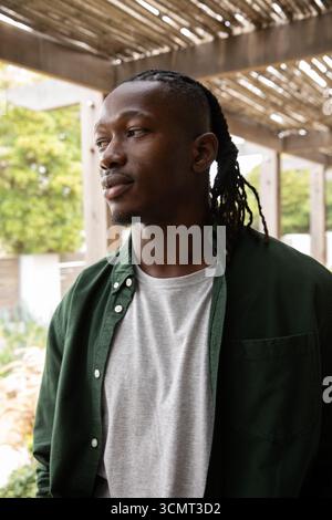 afroamerikaner, der auf der Terrasse unter Pergola steht, zwischen Gartensträuchern, links blickt, Kopierraum Stockfoto