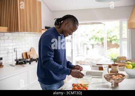 afroamerikaner knackt und rührt Eier auf der Kücheninsel mit einer Glasschale und einem Metallquirl Stockfoto