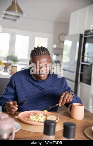 afroamerikaner schneidet Eier und Toast auf einem Teller am Küchentisch mit Pfirsichbecher Stockfoto