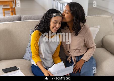 Diverse Mom und Teenager-Tochter sitzen zu Hause auf einem hellen Sofa und lesen Papierbriefe Stockfoto