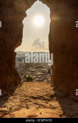 Helles Sonnenlicht, das durch eine enge Öffnung in den alten Burgmauern strömt, erleuchtet eine malerische Stadtlandschaft Stockfoto
