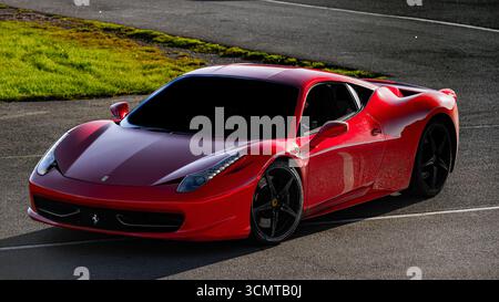 Roter Ferrari 458 Italia Sportwagen auf Asphaltstraße mit schwarzen Leichtmetallfelgen und getönten Fenstern, aus flacher Perspektive fotografiert. Stockfoto