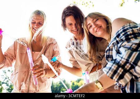 Drei Frauen sind fröhlich dabei, bei hellem, sonnigem Wetter im Freien Blasen zu blasen. Sie wirken entspannt und glücklich und genießen eine gute Zeit, um sich zu entspannen Stockfoto