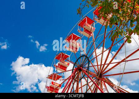 Nahaufnahme eines Riesenrads mit roten Hütten, die sich in einen leuchtend blauen Himmel mit verstreuten weißen Wolken erheben und die pulsierende Stimmung eines Sommeramüsants festhalten Stockfoto