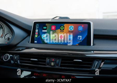 Apple CarPlay-Bildschirm mit Symbolen im modernen Auto. Fahrzeuginnenraum mit Hochglanzholz, Nahaufnahme des Infotainment-Systems. Stockfoto