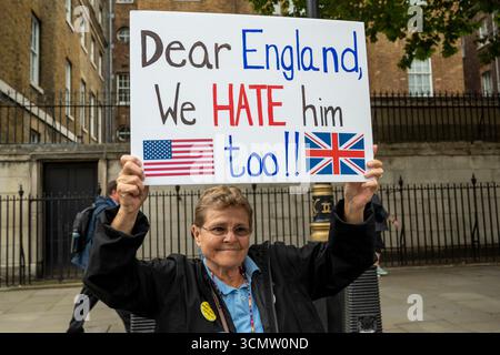Ein amerikanischer Demonstrant gegen den Besuch von Donald Trump in Großbritannien hält ein Plakat mit der Aufschrift "lieber England, wir hassen ihn auch" mit den Fahnen der USA und des Vereinigten Königreichs. Stockfoto