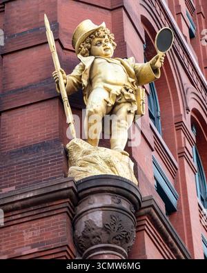 New York, NY - USA - 14. September 2025 Goldene Statue von Puck mit Spiegel und Personal auf dem Puck Building aus rotem Backstein in Manhattan im romanischen Reviv Stockfoto