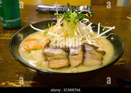 Eine dampfende Schüssel Ramen mit dickem Schweinebauch, Sojasprossen und Gemüse steht auf einem Holztisch in einem Seogwipo Restaurant. Stockfoto