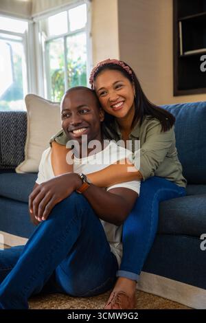 Diverse Paare umarmen sich auf blauem Sofa mit weißem Kissen im Wohnzimmer durch weiß gerahmtes Fenster Stockfoto