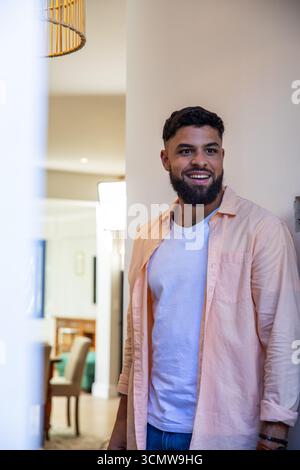 afroamerikanischer Mann, der sich an die Wand im modernen Wohnbereich in der Nähe einer Pendelleuchte lehnt Stockfoto