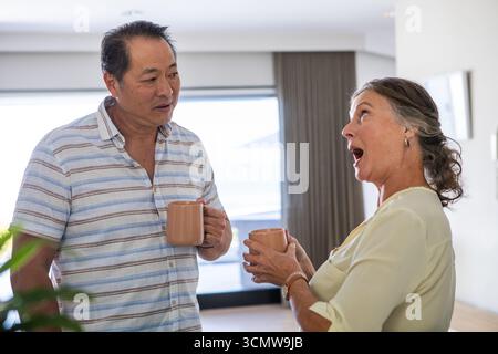 Verschiedene Seniorenpaare stehen im Wohnzimmer und unterhalten sich mit Keramikbecher in der Hand Stockfoto