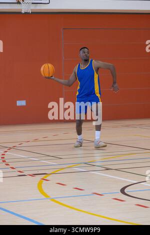 Männlicher Basketballspieler, der auf dem Platz steht, mit Markierungen an der Wand, die den Ball unter dem Rand halten Stockfoto