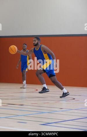 afroamerikanische Mannschaftskameraden dribbeln Basketball auf dem Platz in Uniformen, Kopierraum Stockfoto