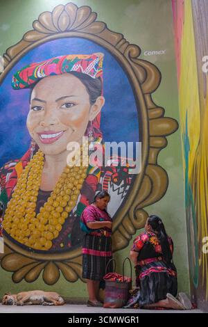 Chichicastenango, Guatemala - 3. Juli 2025: Frauen neben einem Wandgemälde des Künstlers Edwin Gonzalez auf dem Santo Tomas Markt in Chichicastenango, Guatemala. Stockfoto
