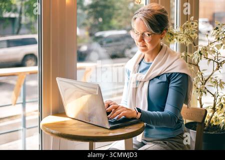 Eine ältere Frau in hellblauem Oberteil und weißem Pullover öffnet die Tür, um nach draußen zu treten Stockfoto