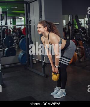 Sportliche junge fitte Frau beim Training mit Kettlebell im Fitnessstudio. Freie Gewichte, Funktionstraining Stockfoto