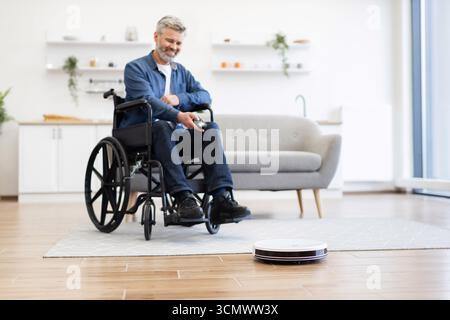 Mann im Rollstuhl mit Roboter-Staubsauger für effiziente Hausreinigung Stockfoto