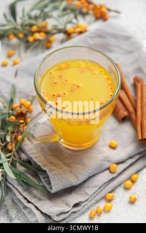 Erfrischender Sanddorntee wird in einem Glasbecher mit frischen Beeren und Zimtstangen serviert Stockfoto