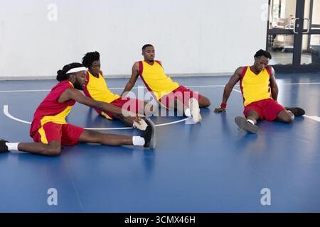 afroamerikanische Männer, die in Trainingstrikots auf dem blauen Basketballfeld die Beine Strecken Stockfoto