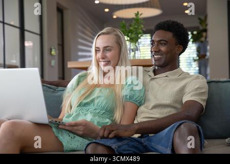 Verschiedene Paare sitzen auf der Couch in blauem Blau und suchen im Wohnzimmer auf einem silbernen Laptop Stockfoto