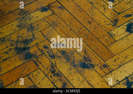 Nahansicht eines Holzbodens mit Fischgrätenmuster. Die Dielen weisen verschiedene Verschleißspuren auf, darunter Kratzer und Verfärbungen Stockfoto