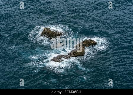 Blick Aus Der Vogelperspektive Auf Felsige Ausläufer, Umgeben Von Weißem Schaum Im Tiefblauen Ozean. Meeresgesteine, die aus Wellen entstehen, Küstenlandschaft, Meeresumwelt Stockfoto